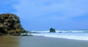Scenic view of Tantadi Beach with black sand, rocky cliffs, and pier near Vizag